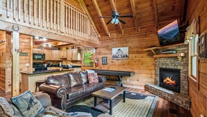 L’intérieur chaleureux d’un chalet avec un canapé en cuir, une cheminée, des murs en bois et un coin cuisine.