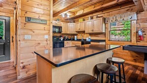 Une cuisine de style rustique, avec des éléments en bois, un îlot central, des tabourets de bar et une fenêtre donnant sur un paysage verdoyant.