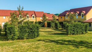 Una hilera de edificios amarillos con tejados rojos, rodeados de setos verdes y césped.