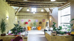 Un interior rústico con vigas de madera a la vista, un área de estar central con sillas coloridas y una variedad de plantas en macetas.