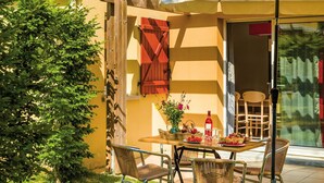 Eine Terrassengruppe im Freien mit Esstisch, Korbstühlen und einer Holzhütte mit weißem Baldachin.