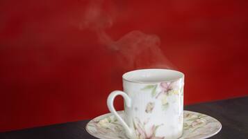 A white ceramic cup with floral designs on a matching saucer, placed on a dark surface against a red background.