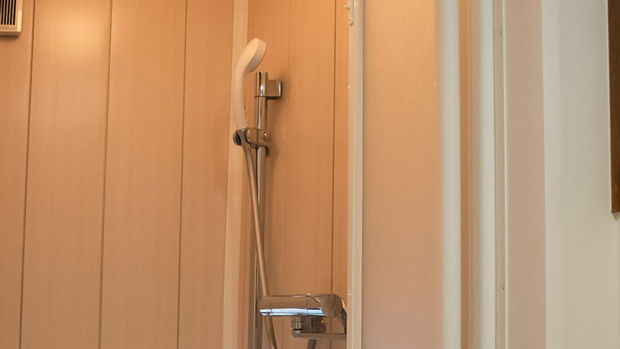 A shower with a handheld showerhead and a wall-mounted control panel.