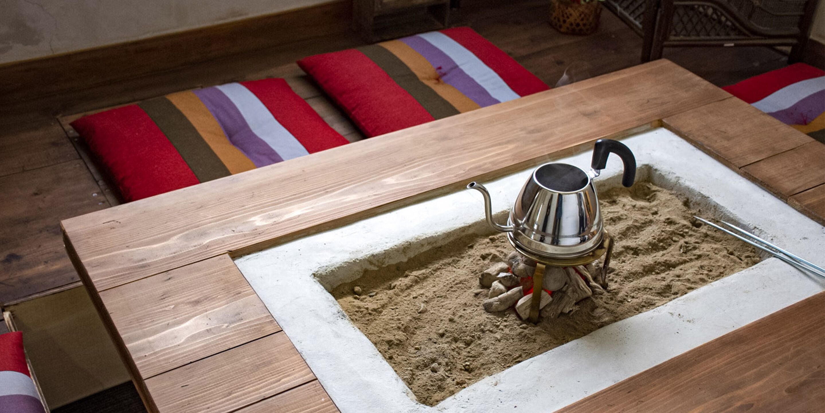 A wooden table with a built-in sand tray and a metal kettle.