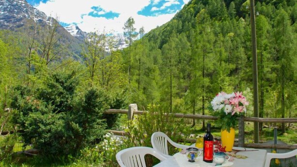 Ein Tisch draußen mit Blick auf Berge, einer Weinflasche und einem Blumenstrauß.