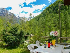 Une table dressée en plein air, avec vue sur les montagnes, une bouteille de vin et un vase rempli de fleurs.