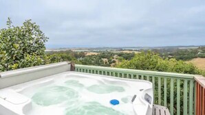 Un bain à remous sur un balcon offrant une vue sur un vignoble et des collines lointaines.