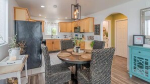 Une cuisine moderne avec des meubles en bois, un réfrigérateur noir et un coin repas comprenant des chaises en osier et une table ronde.