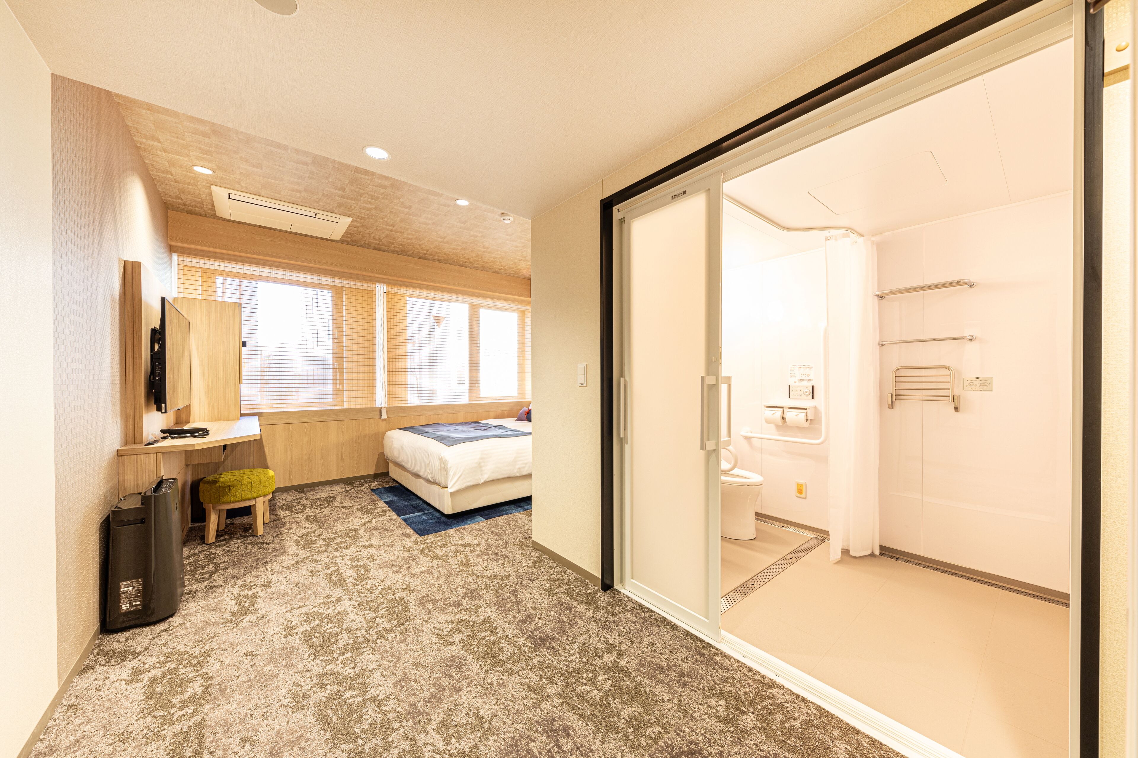 A hotel room with a bed, desk, and a sliding door leading to a bathroom.