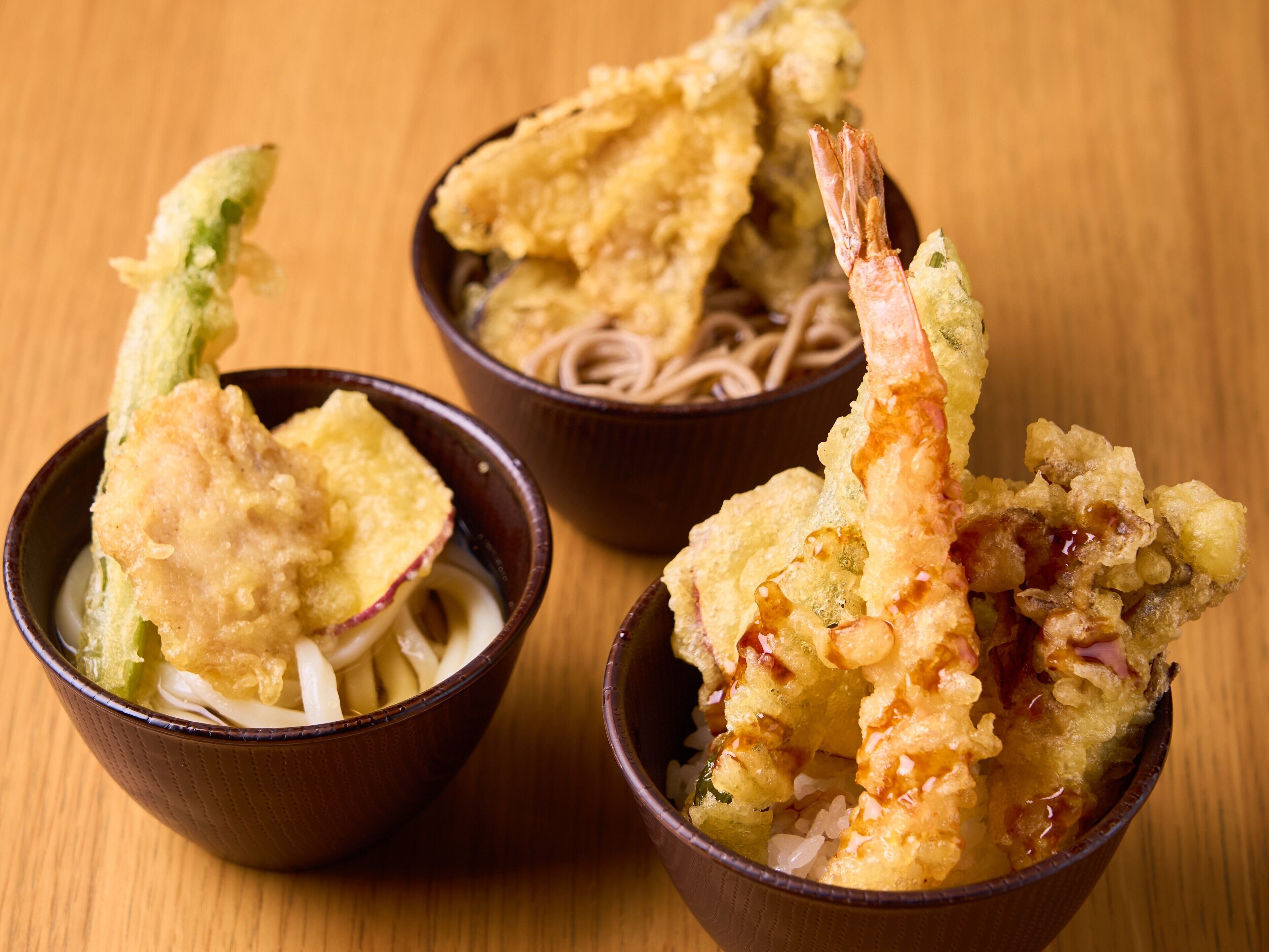 Three bowls of ramen with tempura shrimp and vegetables.