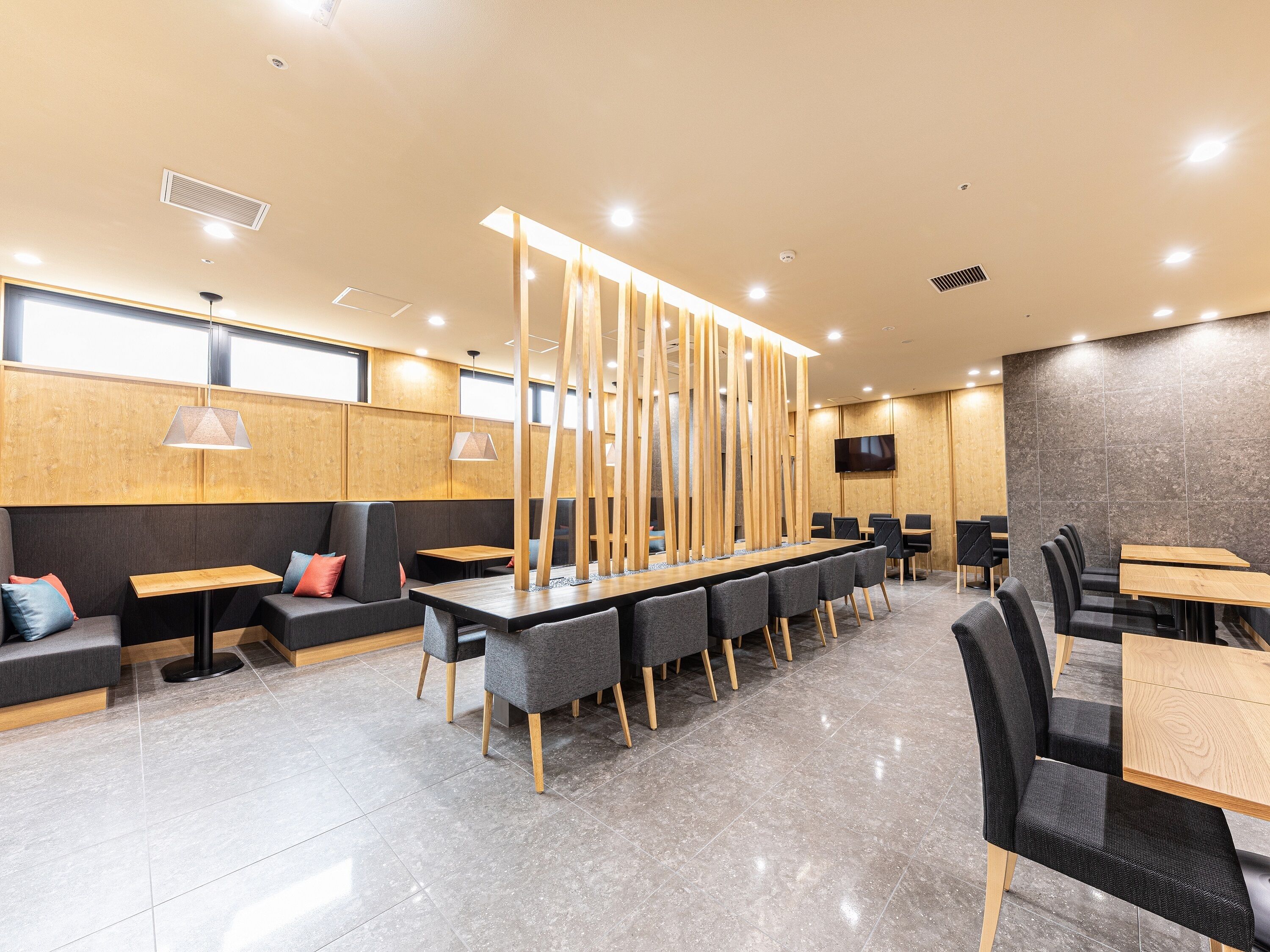 Un restaurante moderno con una mesa larga compartida, asientos individuales y una pantalla de televisión grande.