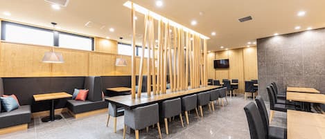Un restaurante moderno con una mesa larga compartida, asientos individuales y una pantalla de televisión grande.