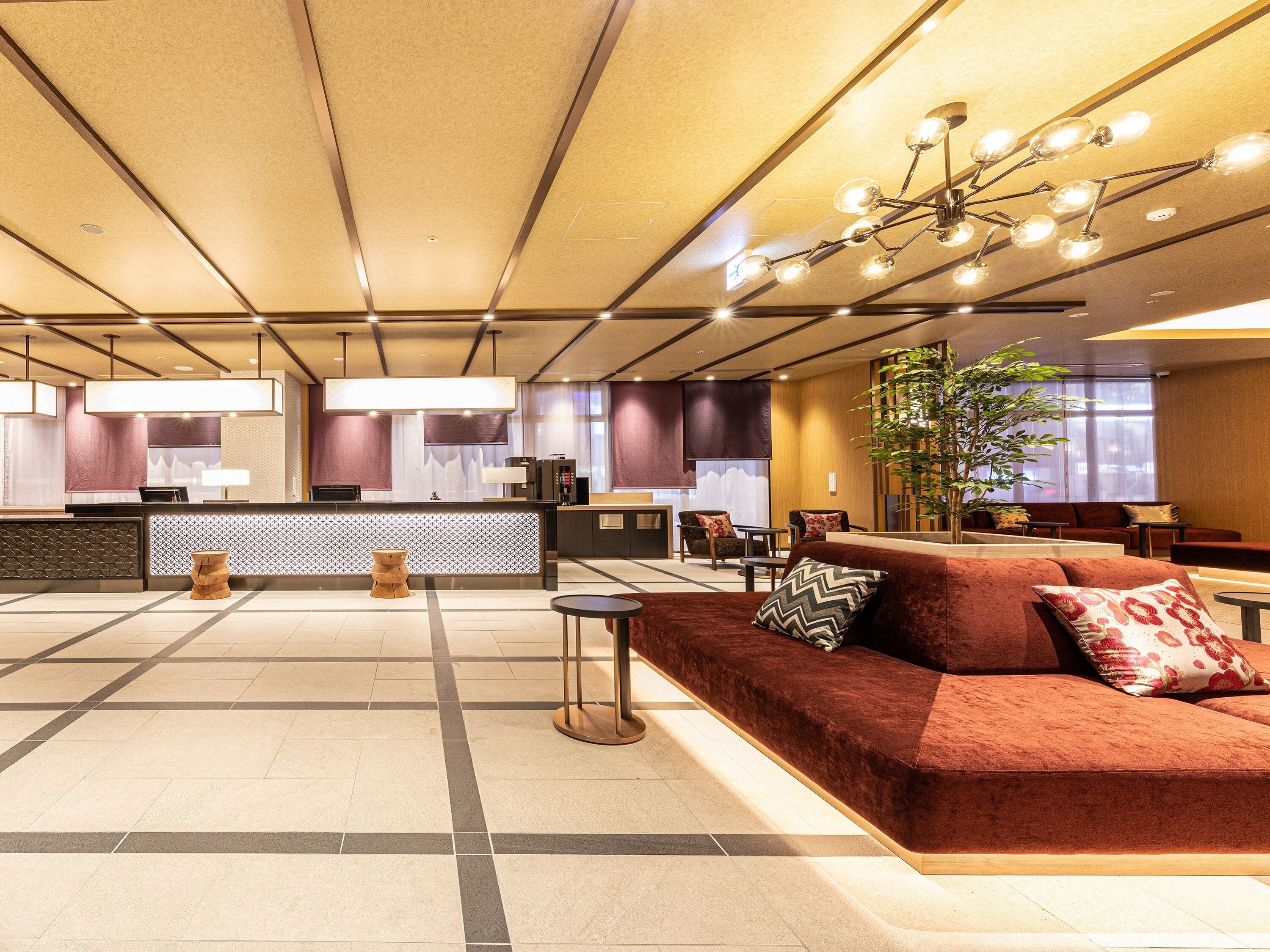 A modern hotel lobby with a reception desk, seating area, and a large plant.