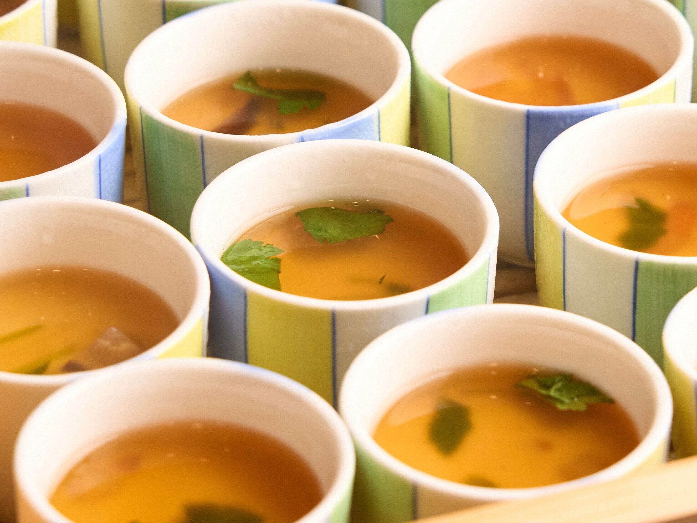 Multiple cups of soup with mint leaves, arranged in a row.