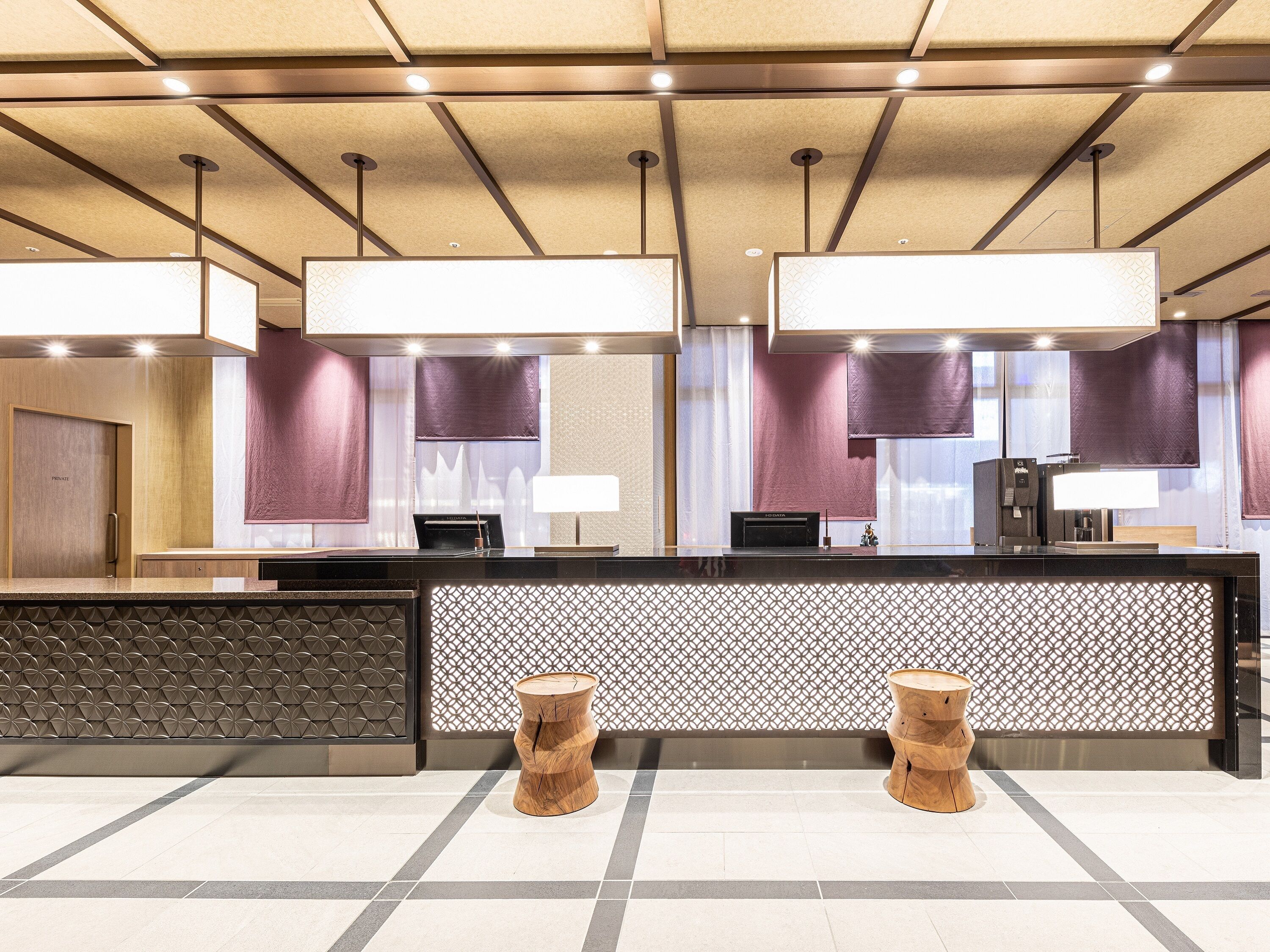 A modern reception area with a reception desk, two wooden stools, and a patterned wall.