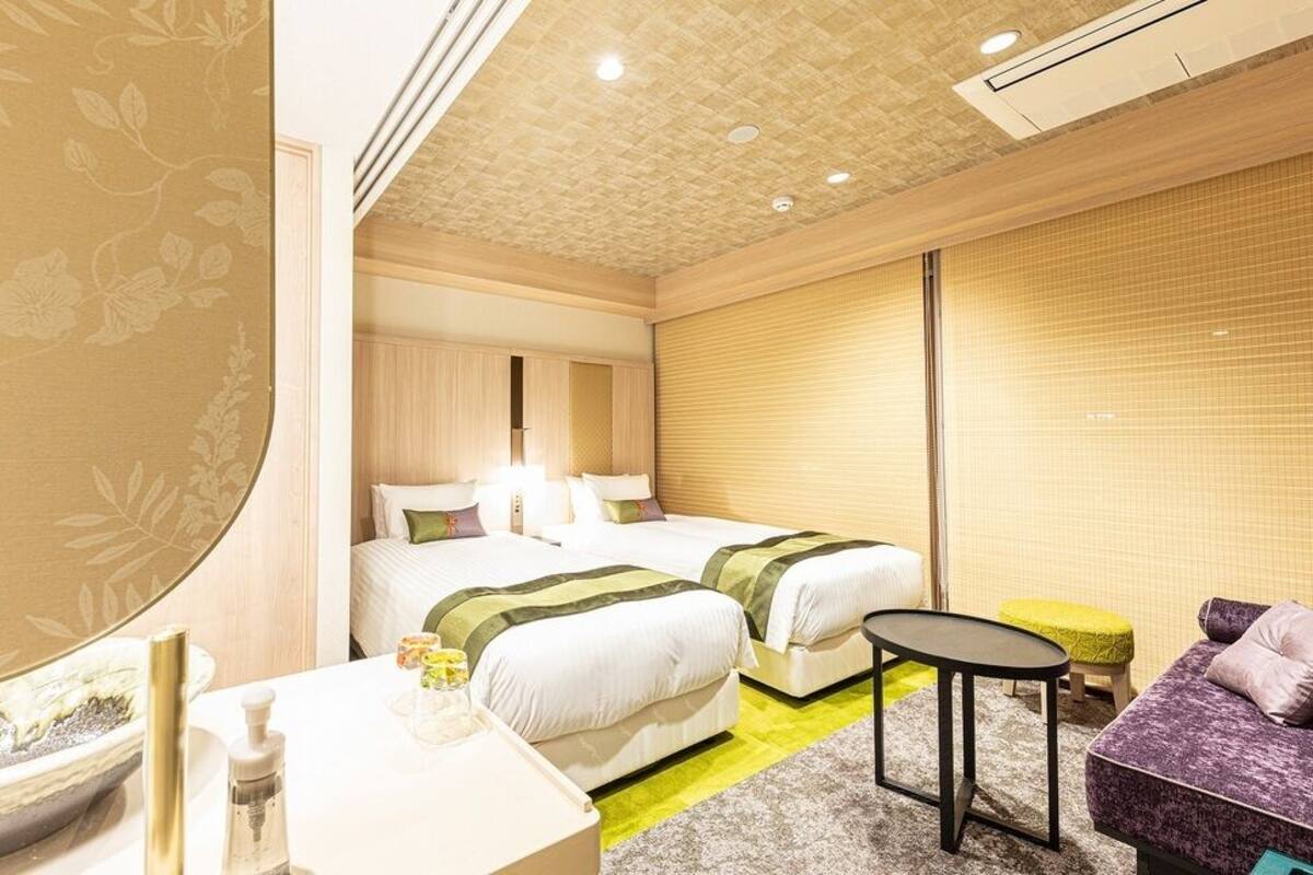 Ein Hotelzimmer mit zwei Betten, einem kleinen Tisch, einer Couch und einem großen Spiegel.