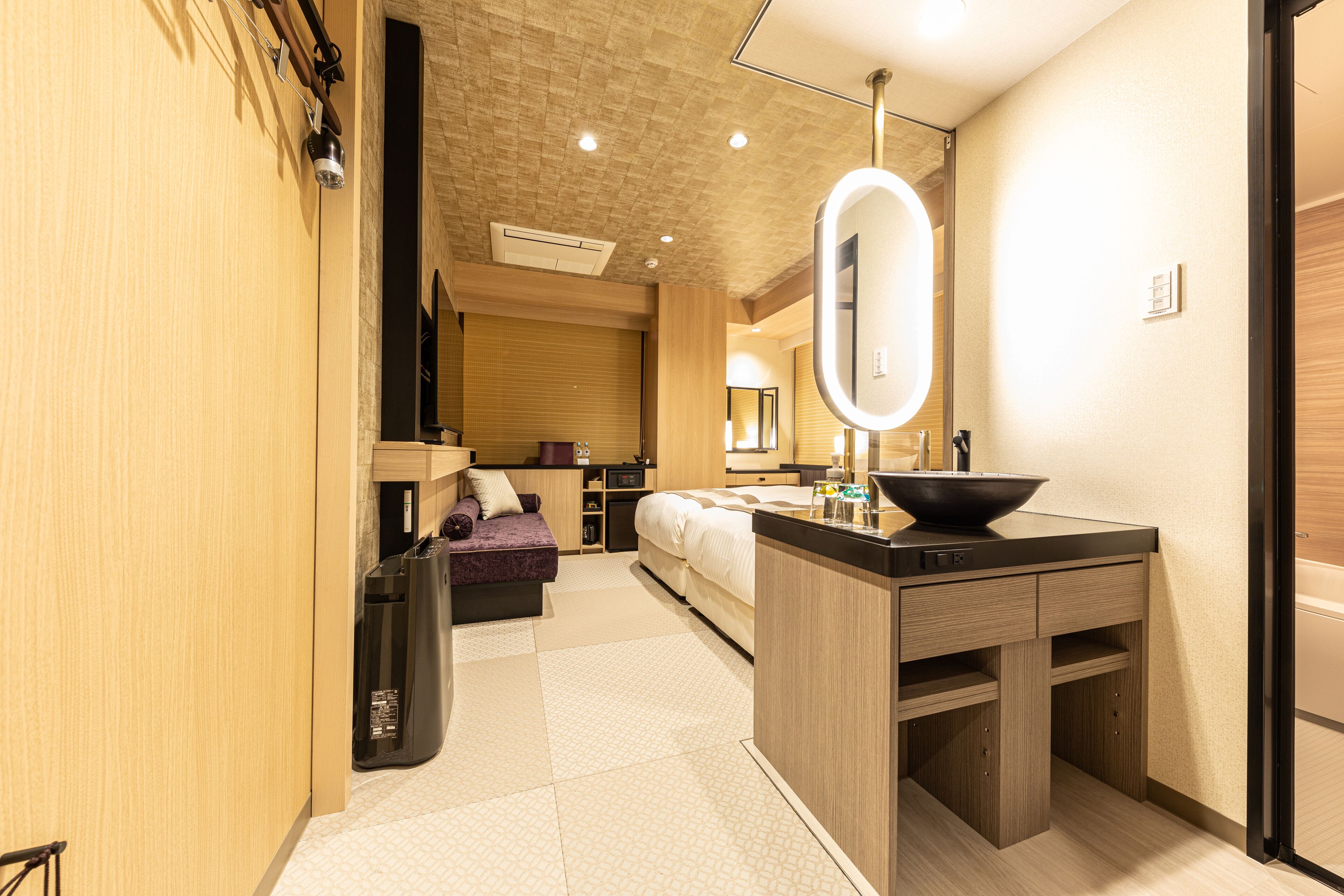 Una habitación de hotel moderna con kitchenette, un espejo grande, un sofá y una cama.