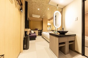 A modern hotel room with a kitchenette, a large mirror, a sofa, and a bed.