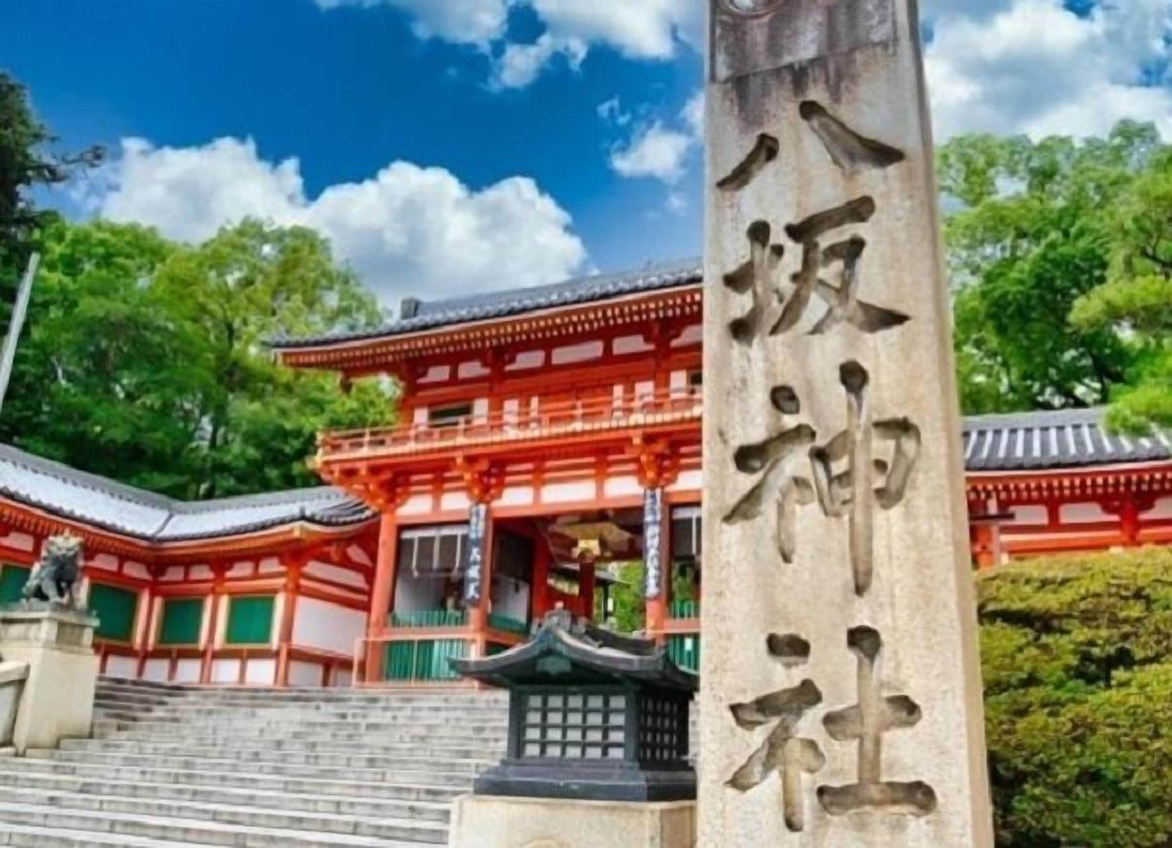 Un edificio tradicional japonés con fachada roja y verde, un monumento de piedra con caracteres japoneses y una escalera que lleva a la entrada.