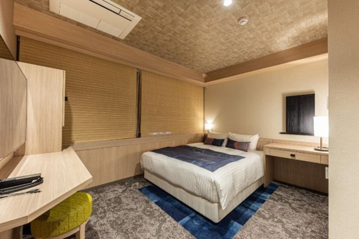 Una habitación de hotel moderna con cama, mesita de noche, escritorio y una pequeña zona de estar.