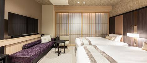 Habitación de hotel con dos camas, un sofá, un televisor y una ventana con persianas verticales.