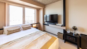 A hotel room with a large bed, a TV mounted on the wall, a bedside table with a lamp, and a small mirror.