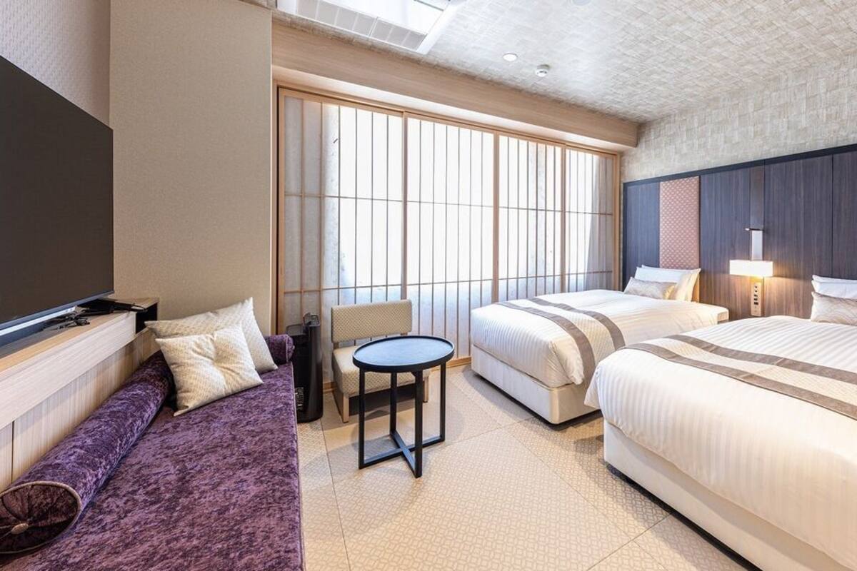 Ein Hotelzimmer mit großem Fenster, einer Couch, zwei Betten und einem kleinen Tisch.
