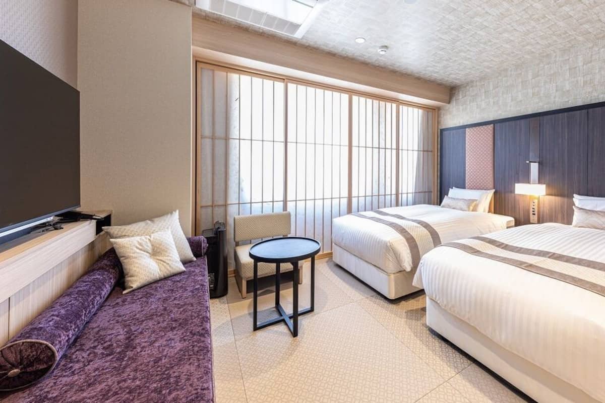 Quarto de hotel com uma janela grande, um sofá, duas camas e uma mesa pequena.
