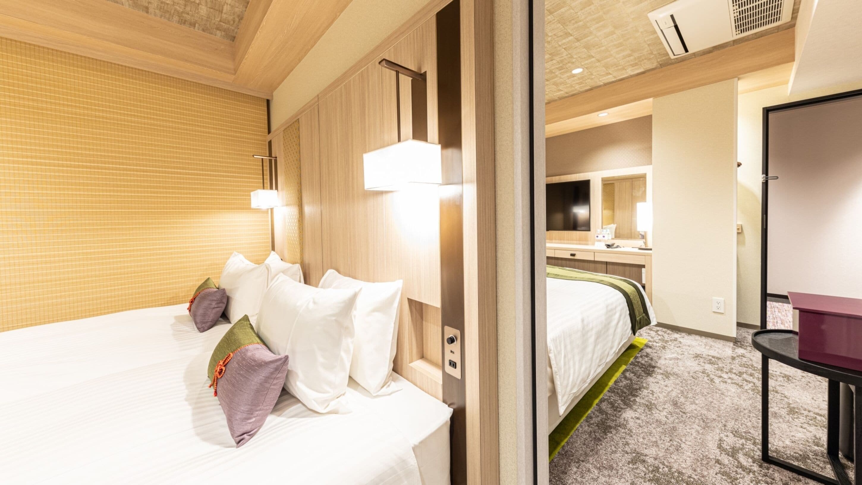 Quarto de hotel com uma cama grande, uma mesinha de cabeceira, um espelho e uma pequena escrivaninha.