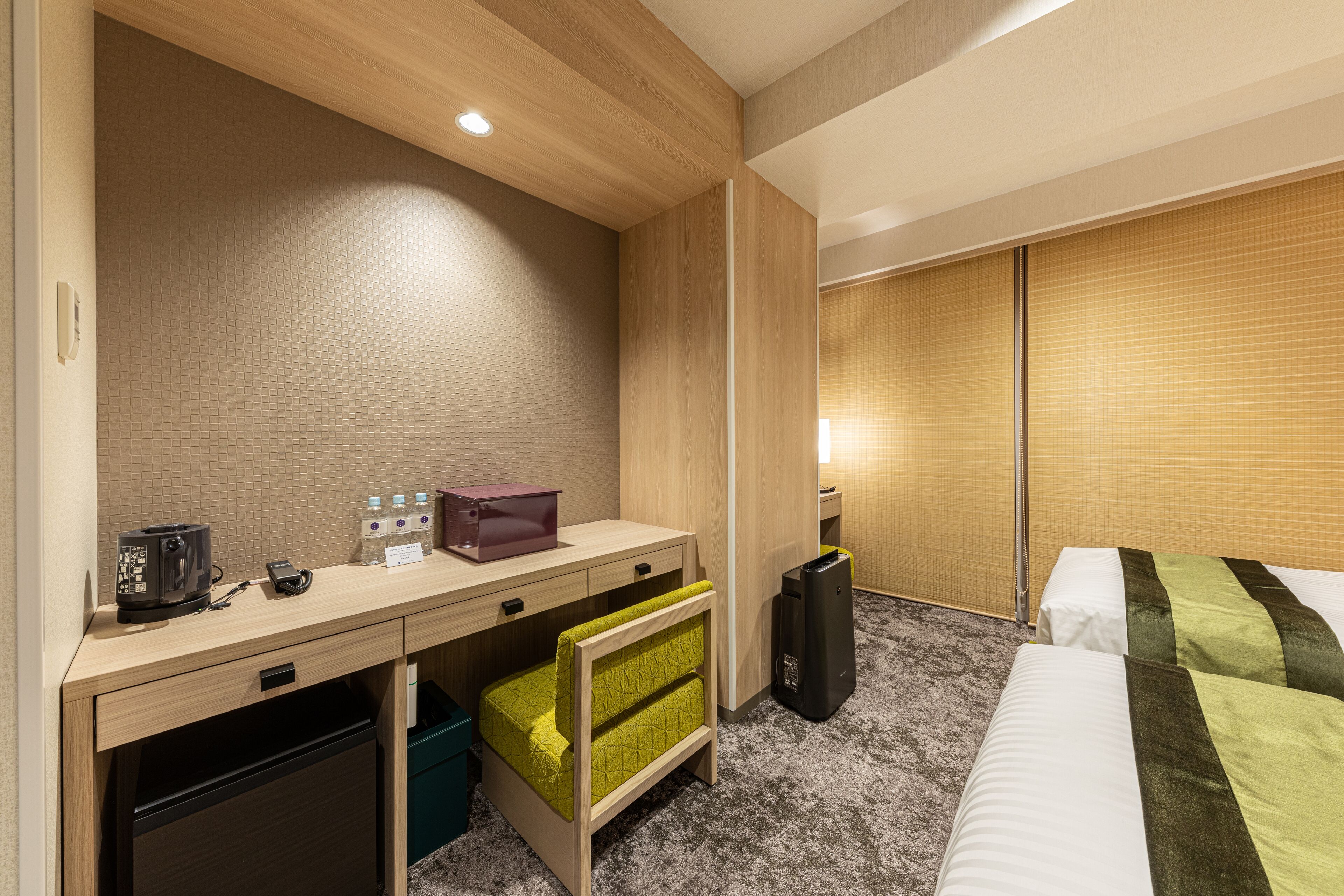 A hotel room with a desk, a small kitchenette, a bed, and a wardrobe.