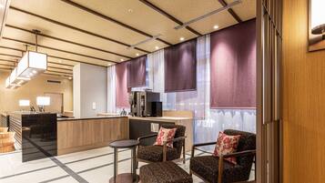 A modern hotel lobby with a reception desk, seating area, and a large window with curtains.