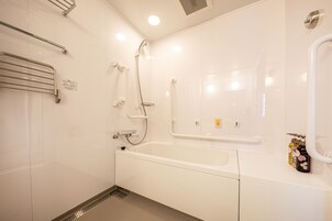 A modern bathroom with a white bathtub, grab bars, and a shower area.