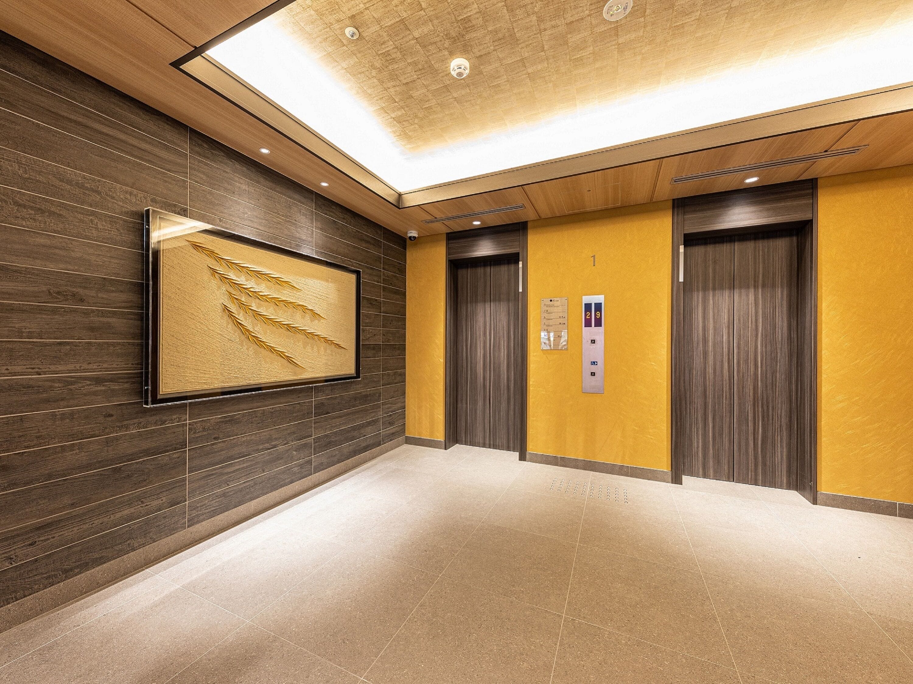 A modern elevator area with a wooden panel wall, a framed artwork, and a floor with a light brown tile pattern.