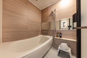 A modern bathroom with a freestanding bathtub, a handheld showerhead, a small stool, and a shelf with toiletries.