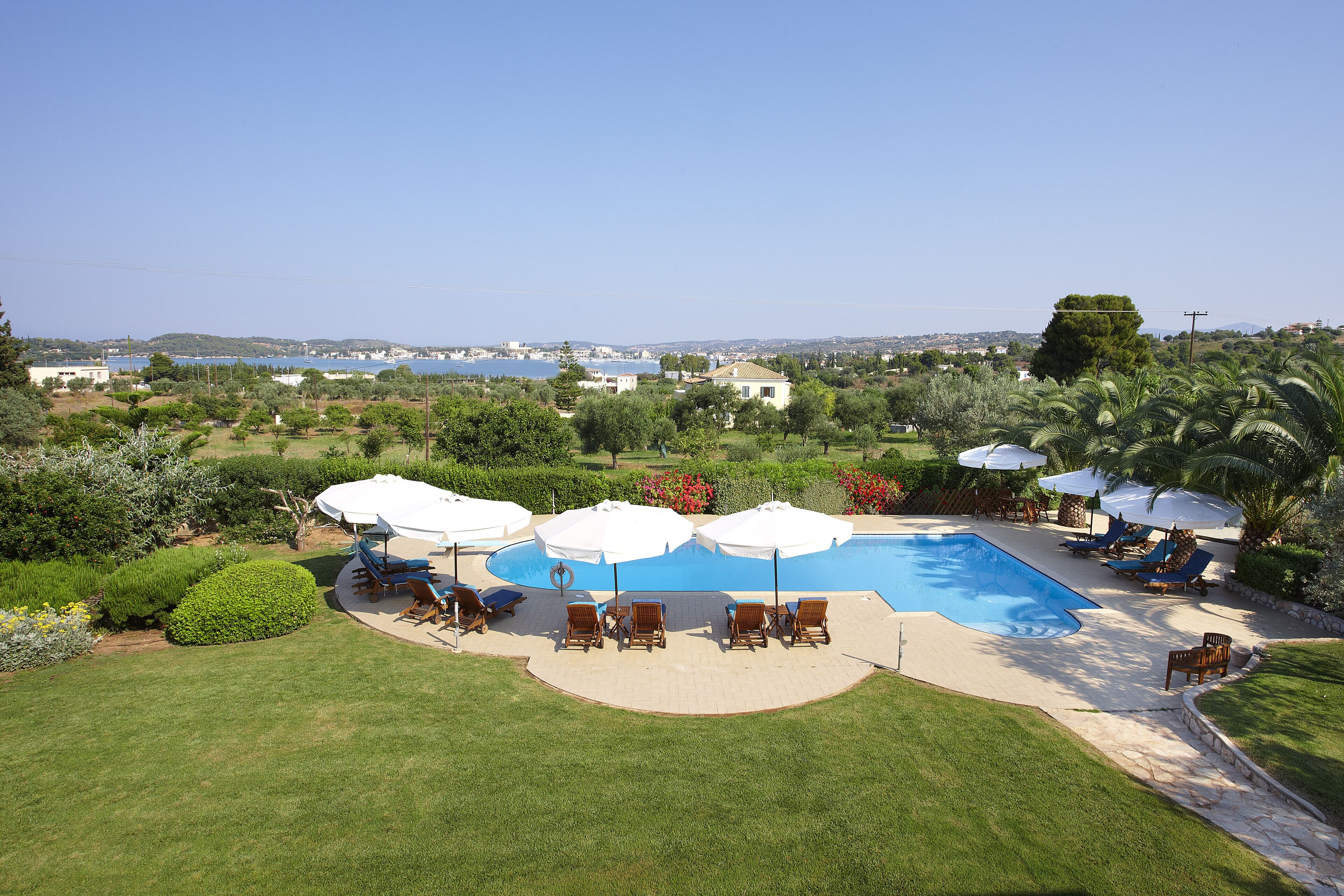 A swimming pool with lounge chairs and umbrellas, surrounded by well-maintained lawns and trees.