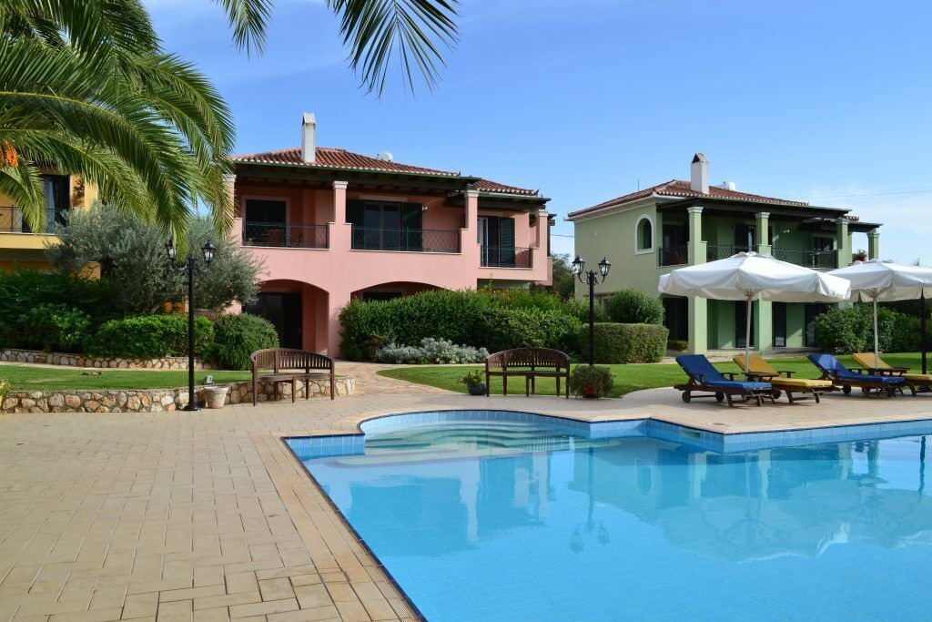 A swimming pool with lounge chairs and umbrellas, surrounded by a brick patio and greenery.