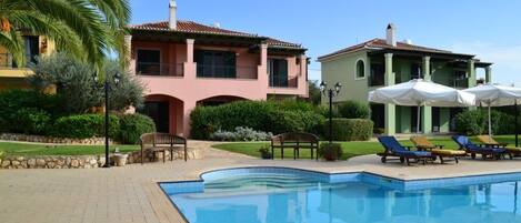 A swimming pool with lounge chairs and umbrellas, surrounded by a brick patio and greenery.