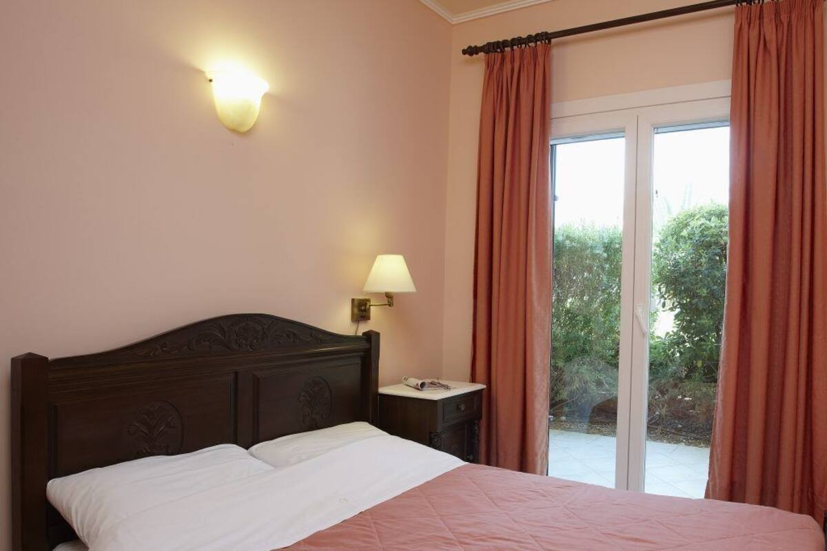 Une chambre d’hôtel avec un lit, une table de chevet, une lampe et une vue sur la verdure, visible à travers une porte-fenêtre coulissante.