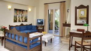 A room with a blue sofa, a wooden desk, a television, and a balcony with curtains. - Nymfes Villas (Ermionida)