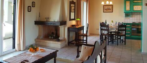 A dining area with a fireplace, a table set with a placemat, and a view into the kitchen.