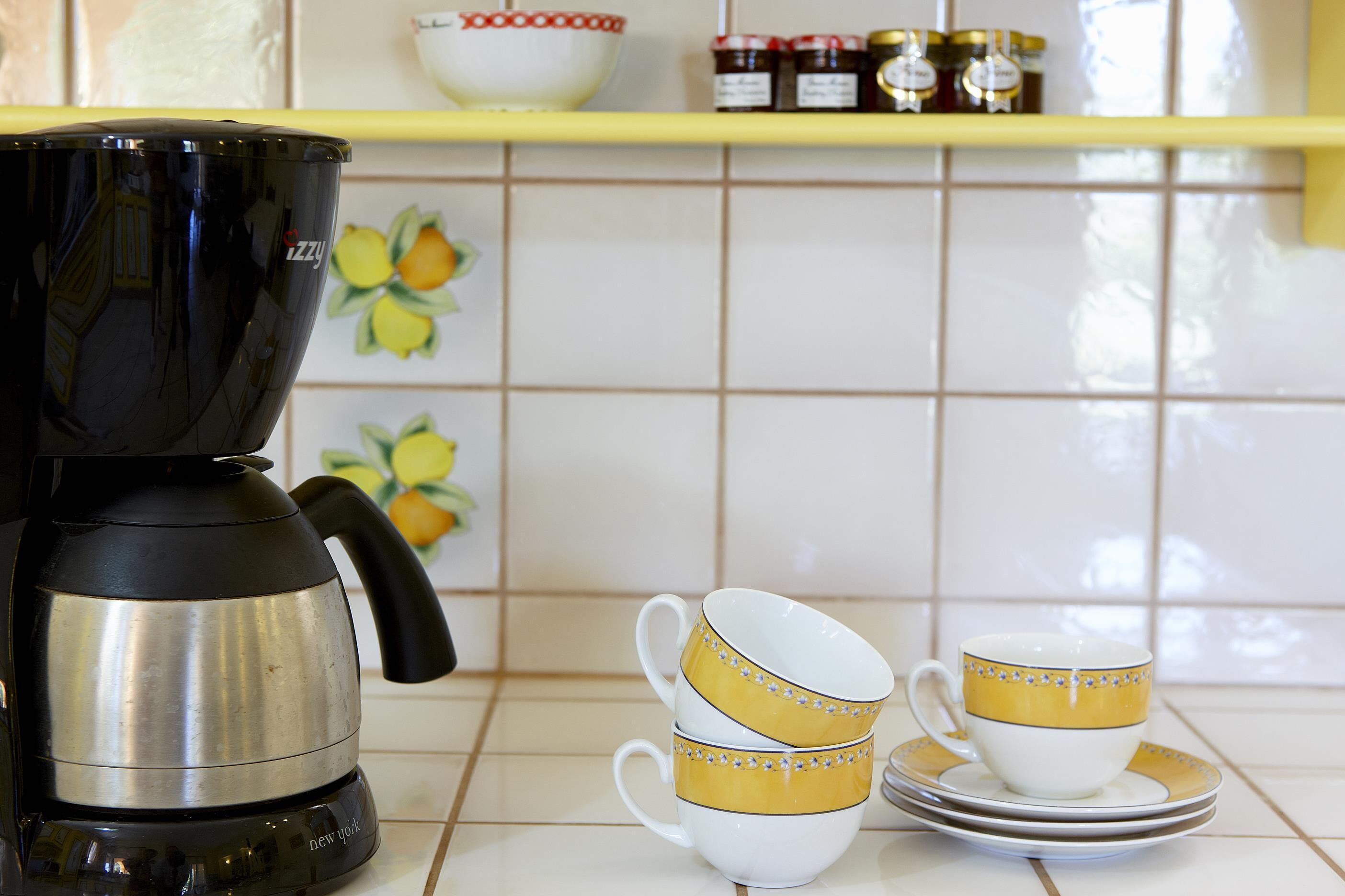 A kitchen with a coffee maker, two stacked cups, and a shelf with jars.