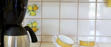 Een keuken met een koffiezetapparaat, twee gestapelde bekers en een plank met potten.