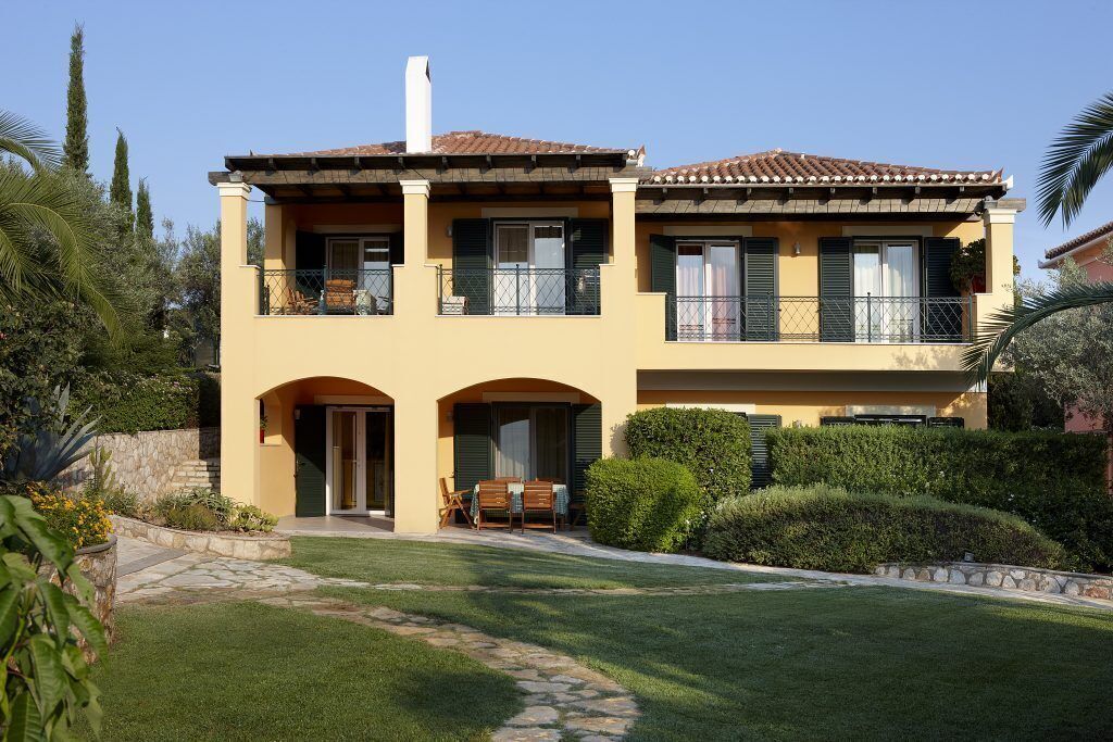 Ein zweigeschossiges Haus im mediterranen Stil mit einer Steinaußenfassade, einem Balkon mit schmiedeeisernem Geländer und einem gepflegten Garten.