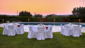 A formal outdoor dining setup with tables and chairs, a pool in the background, and a sunset sky. - Nymfes Villas (Ermionida)