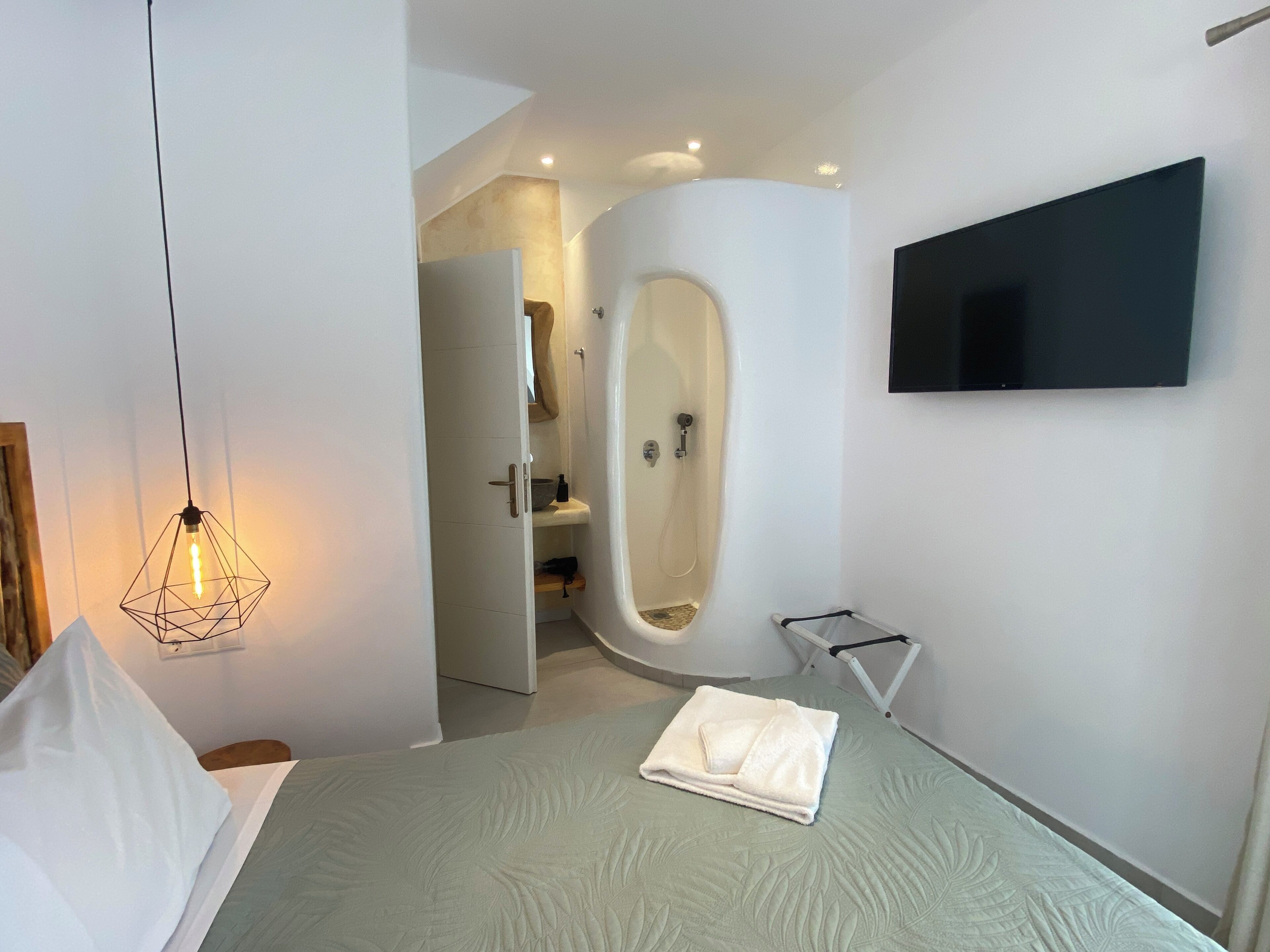 Una camera da letto moderna con un letto, una TV a parete, un angolo doccia e una lampada a sospensione.