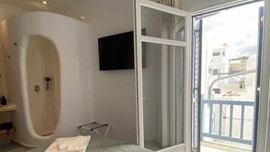 Ein Schlafzimmer mit einer großen Badewanne, einem Bett mit grüner Bettdecke und einem Balkon mit Blick auf Gebäude.