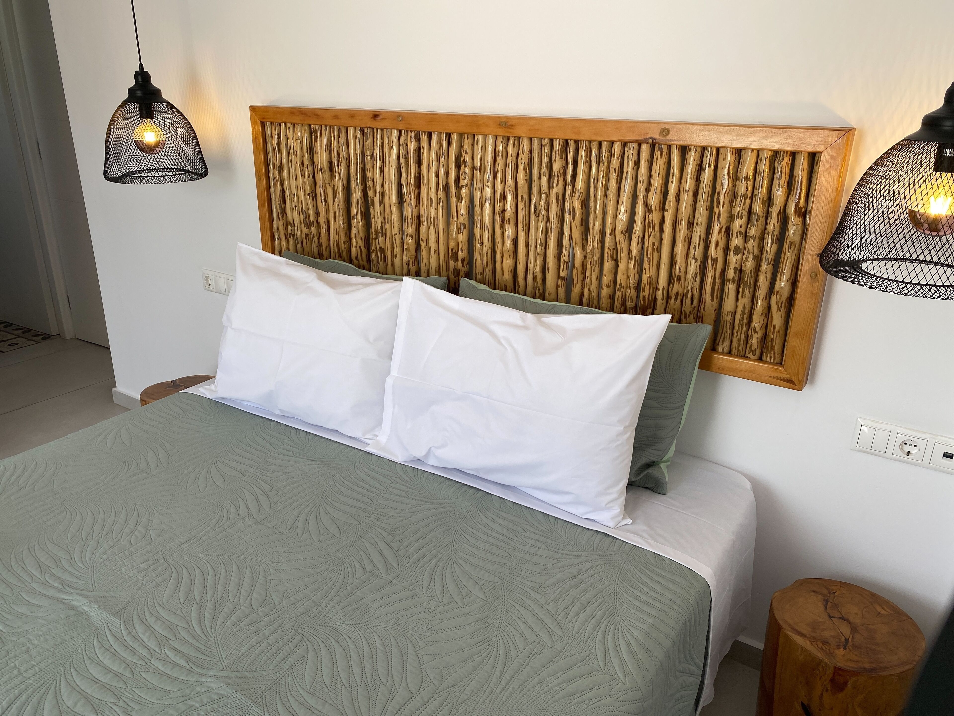 A bed with a textured green bedspread, two white pillows, and a wooden headboard with vertical slats.