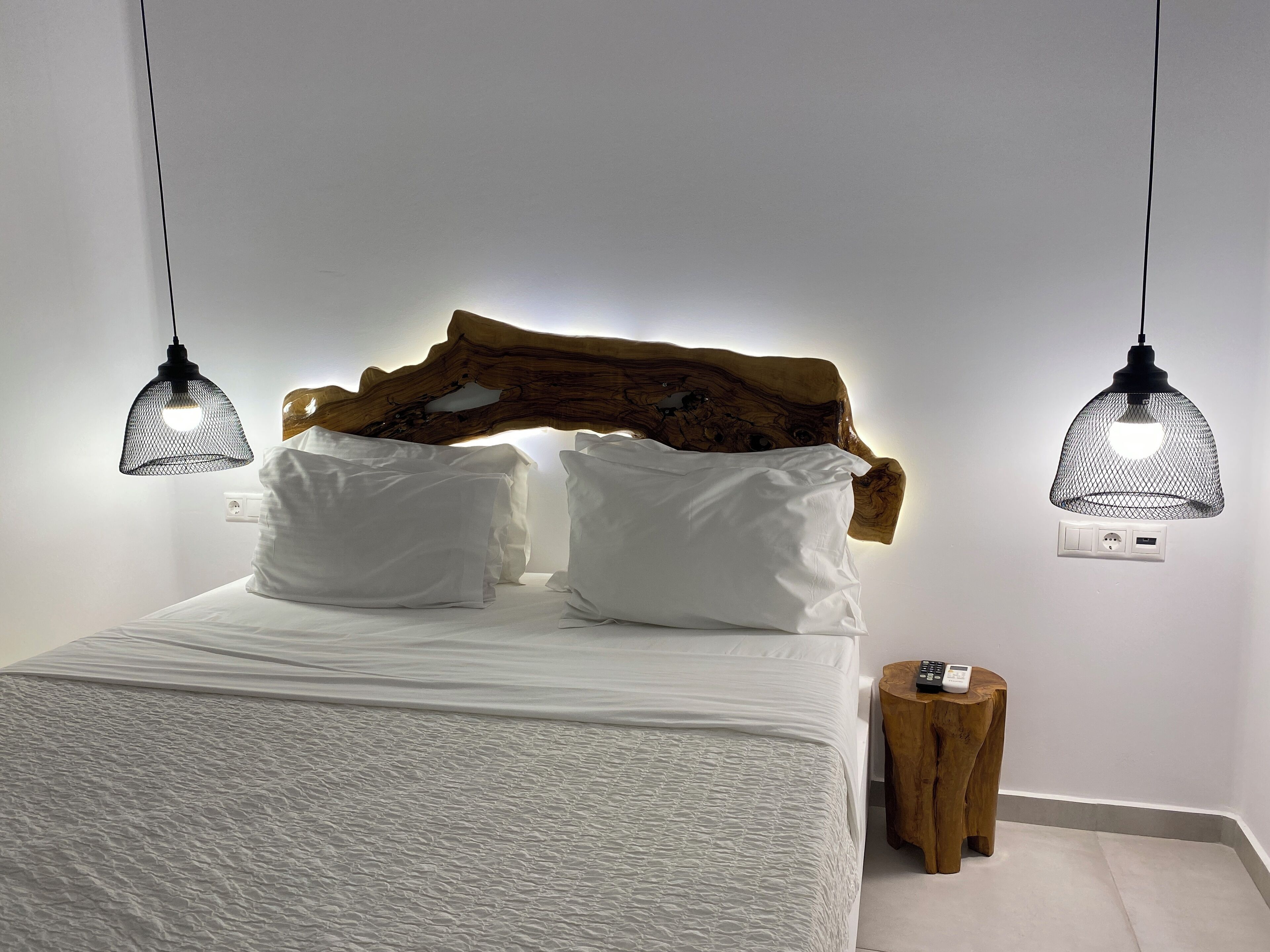 A bed with a wooden headboard, two black pendant lights, and a small wooden stool.