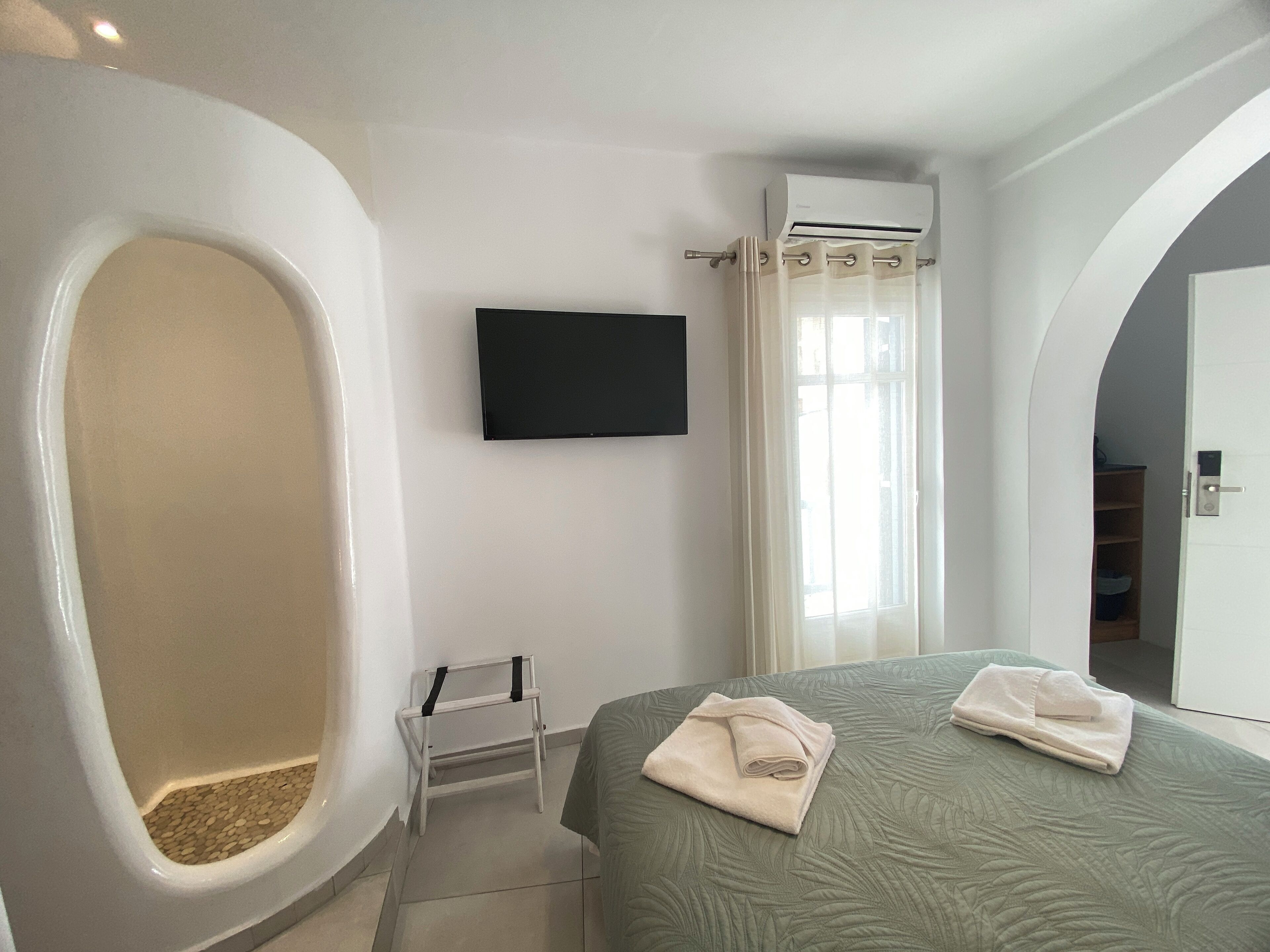 A modern bathroom with a bathtub, a shower, a toilet, a TV mounted on the wall, and a bed with towels.