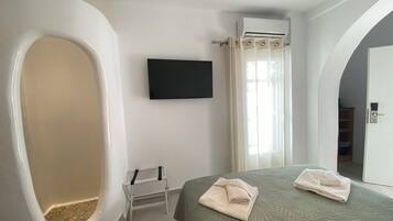 A modern bathroom with a bathtub, a shower, a toilet, a TV mounted on the wall, and a bed with towels.